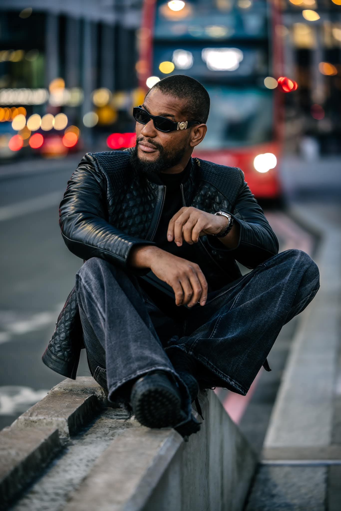 Alexx Ekubo posing in a black leather outfit during a city photoshoot